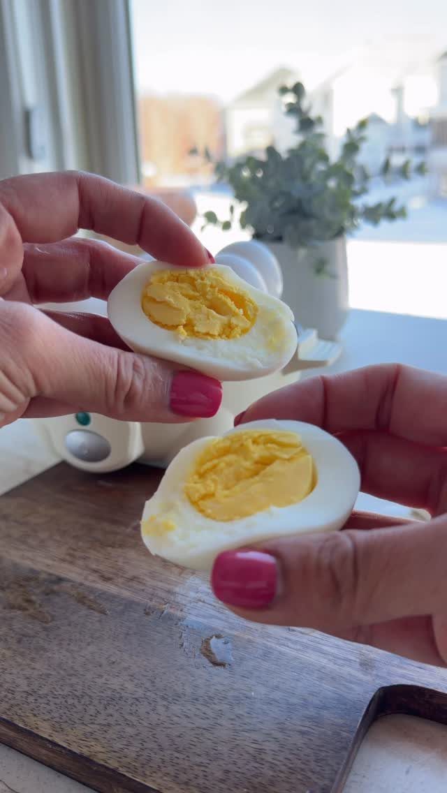 Two halves of a hard boiled egg held over a wooden board.