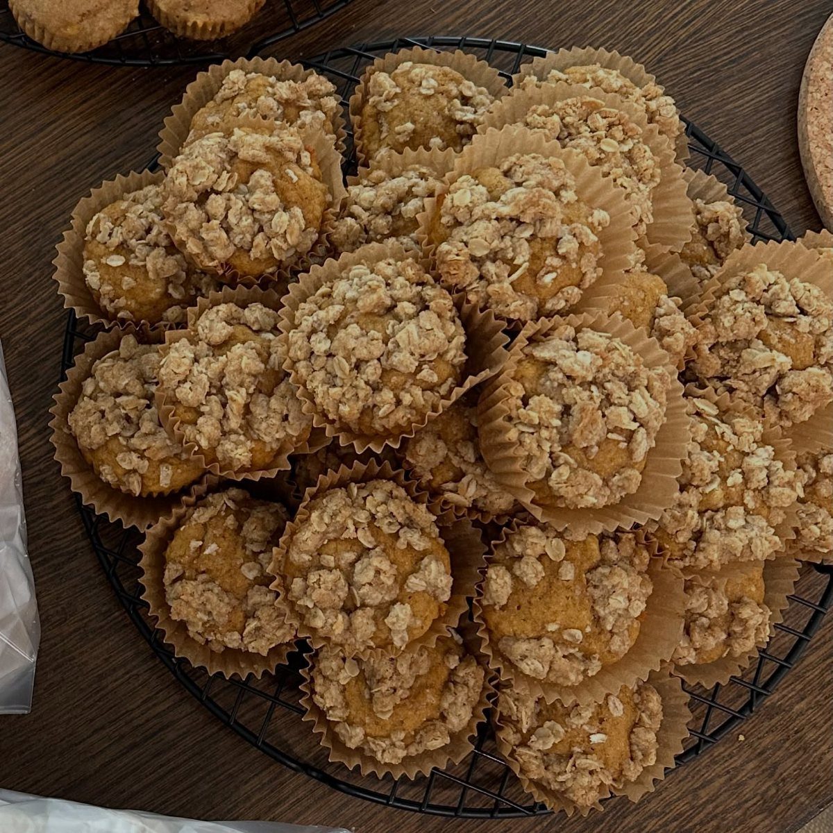Orange-brown muffins with oat crumble toppings on a black wire cooling rack.
