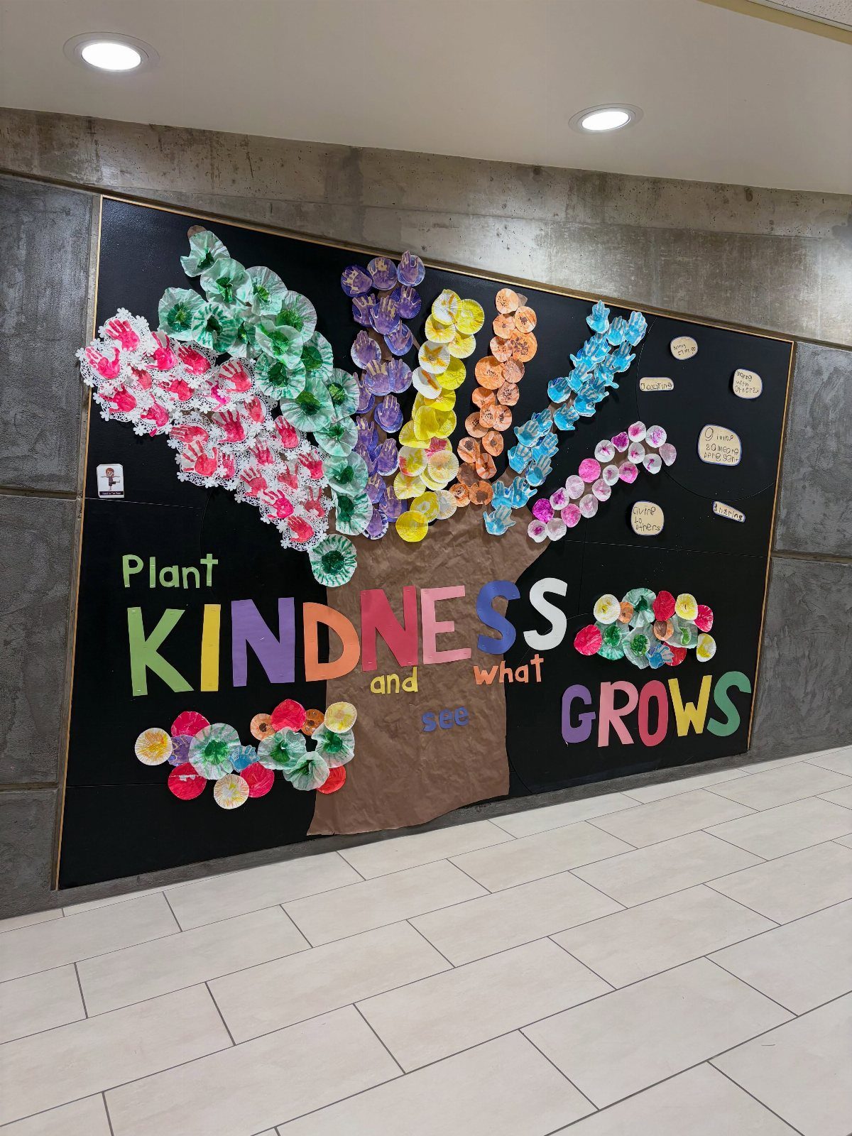Kindness tree bulletin board with colorful cupcake liner leaves and motivational text.