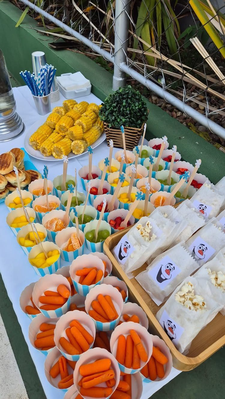 Party food spread with corn, baby carrots in cups, and bagged popcorn.