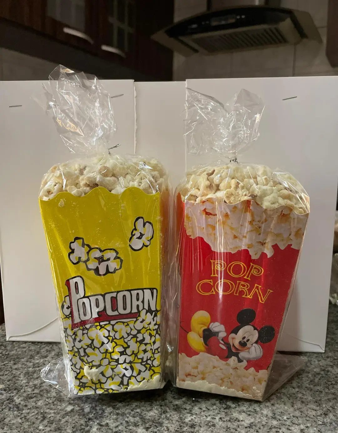 Two popcorn containers wrapped in plastic bags on a grey granite countertop.