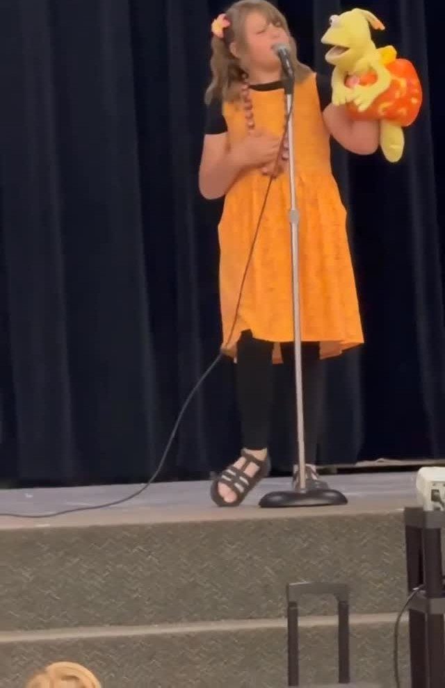 Young girl performing with a puppet and microphone on a stage with black curtains