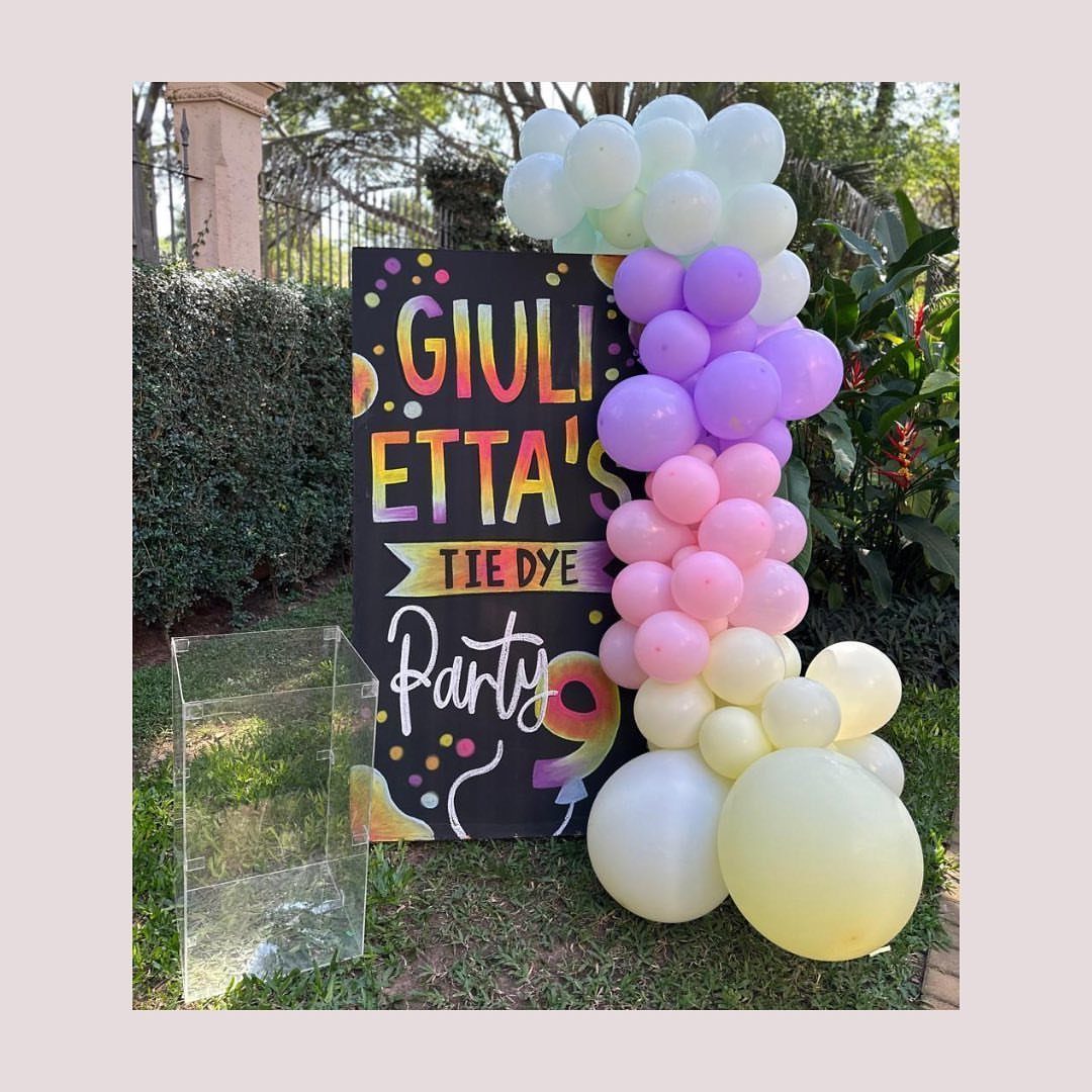 Tie dye party sign with a pastel balloon arch on a green lawn