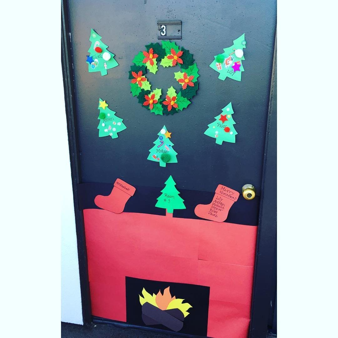 Christmas decorated door featuring a red paper fireplace, stockings, and a green wreath.