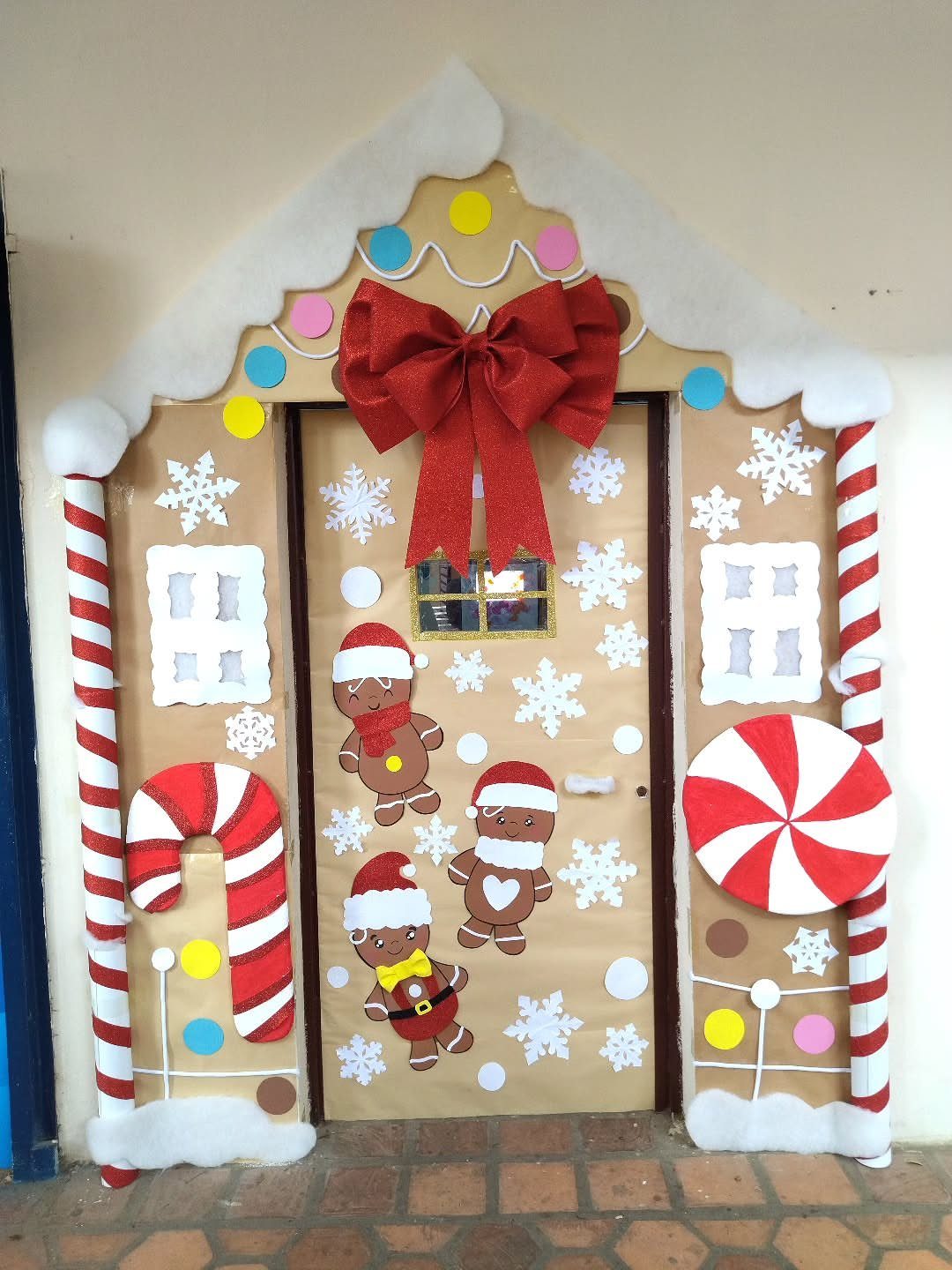 Gingerbread house door decoration with red bow, candy canes, and gingerbread men figures.