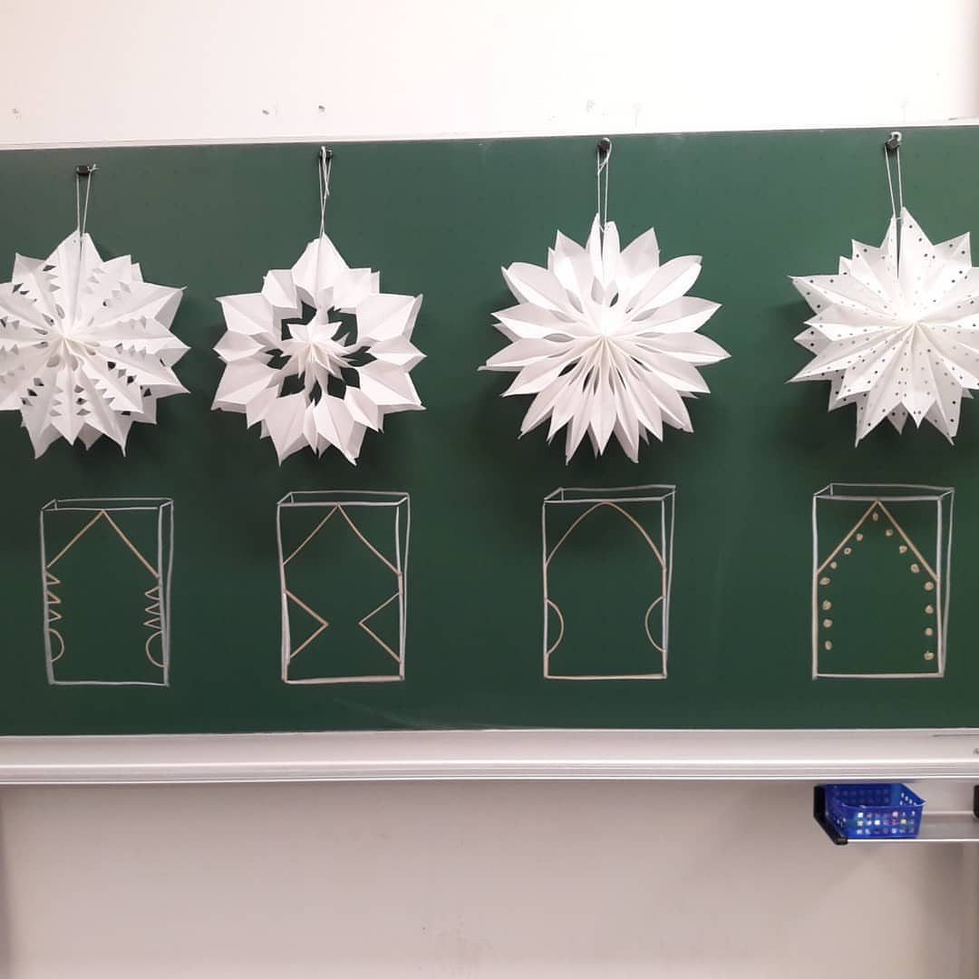 White 3D paper snowflakes hanging against a green chalkboard with chalk drawings.