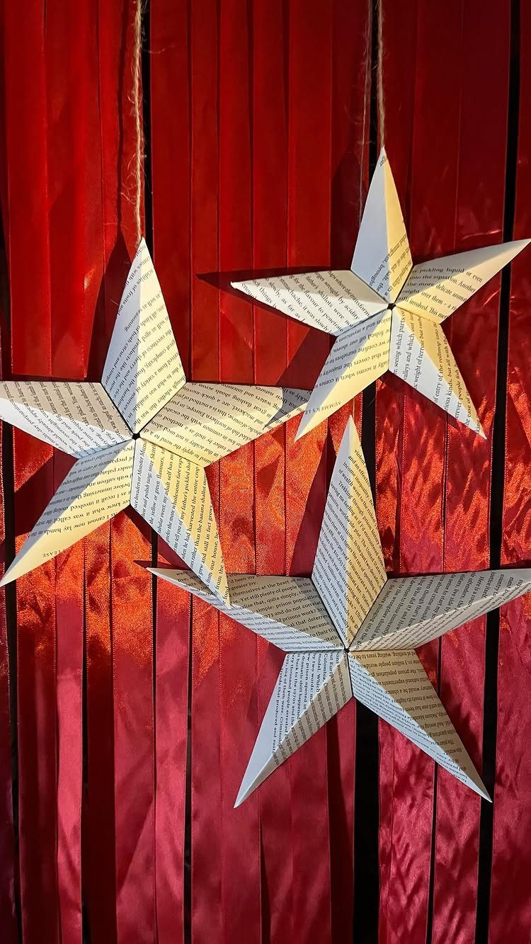Three 3D stars folded from book pages hanging against red fabric strips.