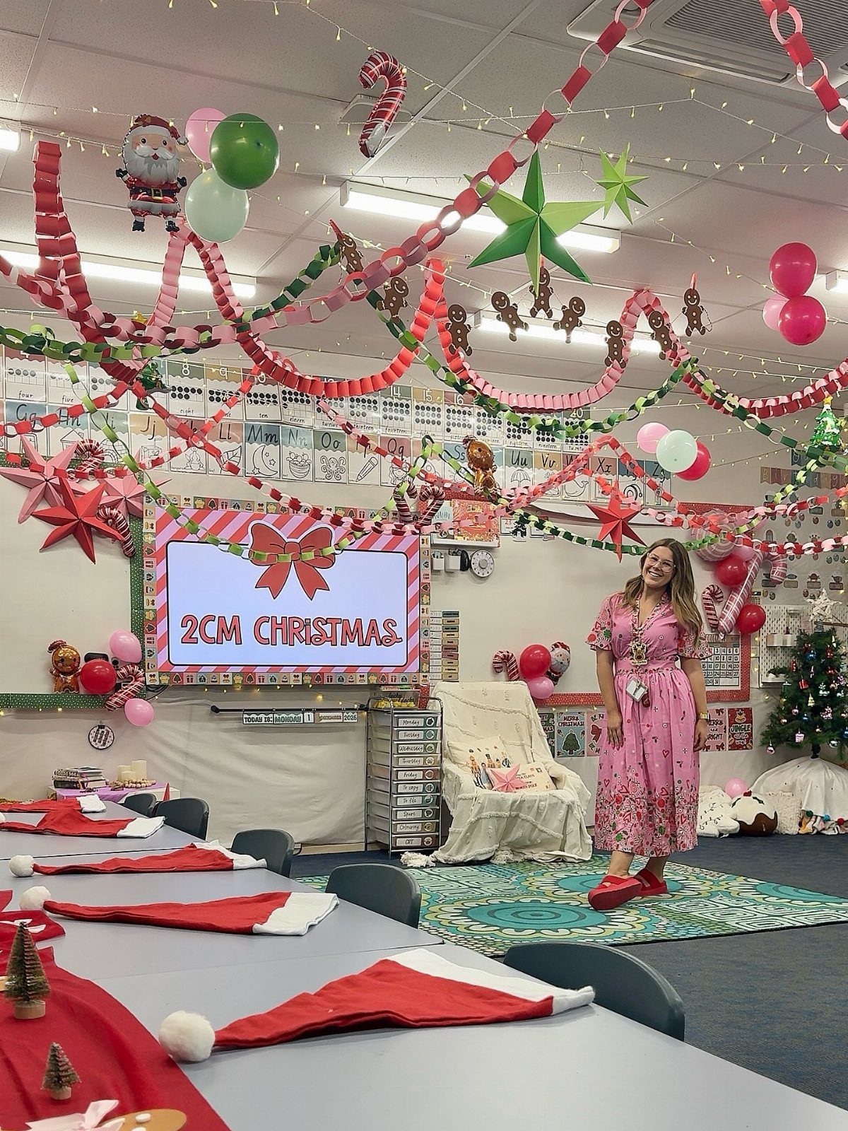 Woman standing in a classroom decorated with Christmas paper chains, stars, and balloons.