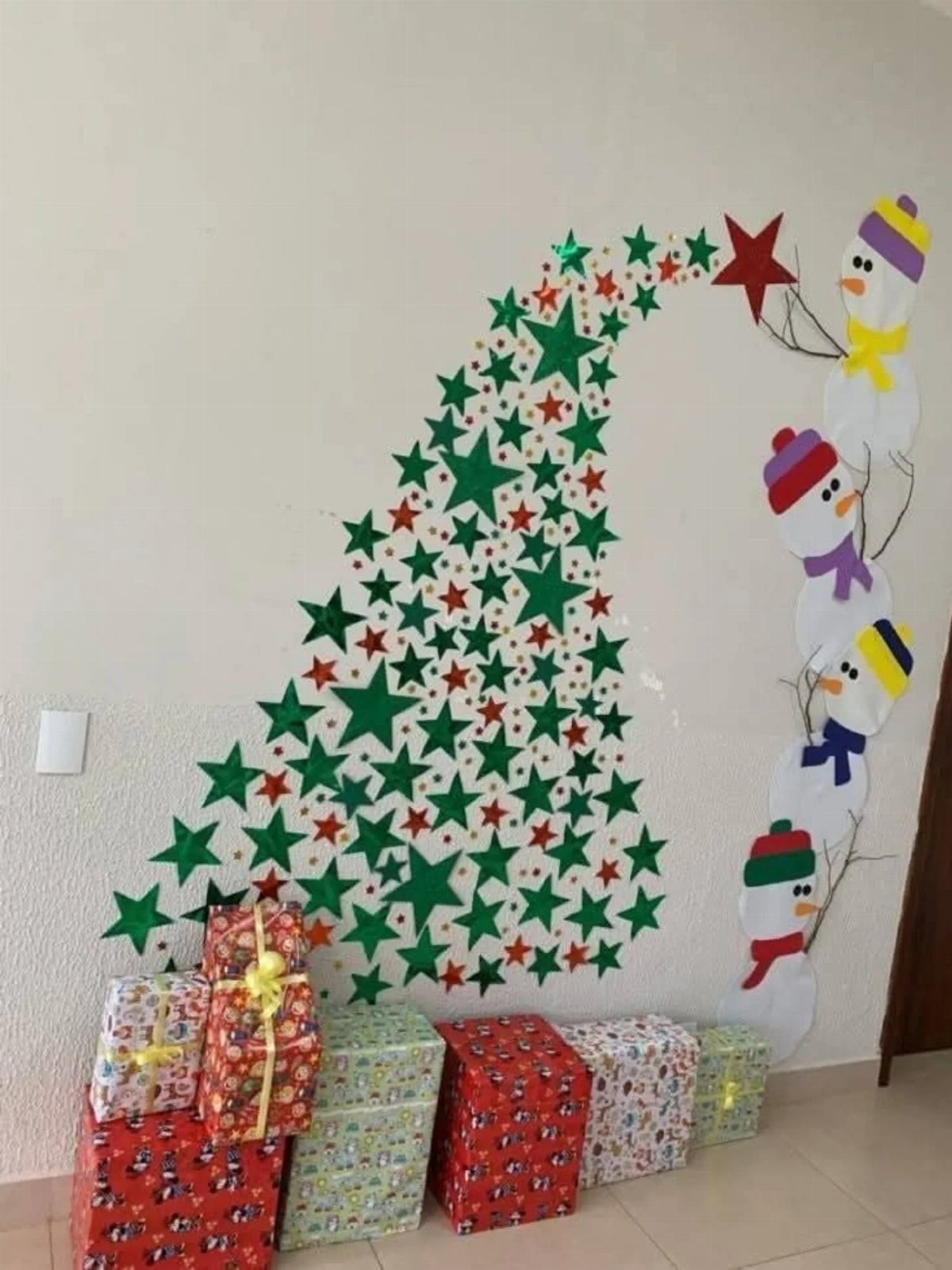 Paper star Christmas tree and snowman decoration on a wall with wrapped gifts