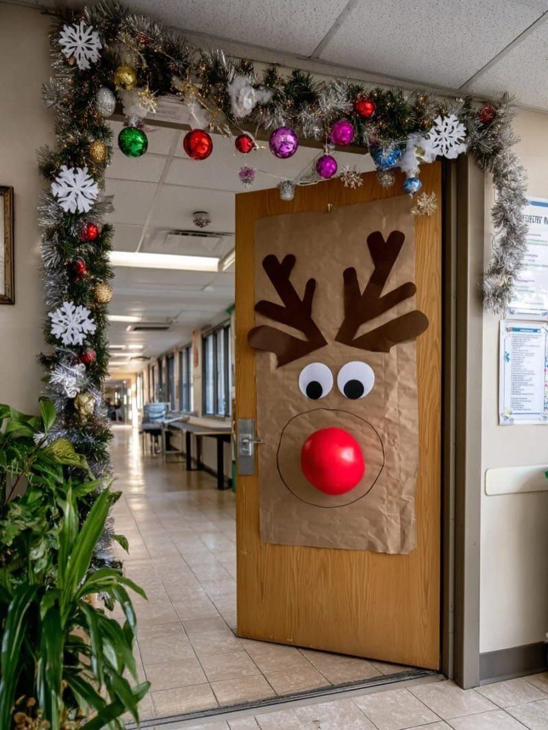 Rudolph the Red-Nosed Reindeer face decoration on a wooden door with festive tinsel.