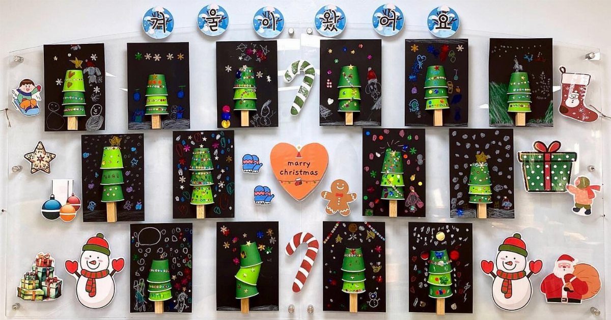 Children's Christmas art featuring 3D paper trees and holiday characters on a wall.
