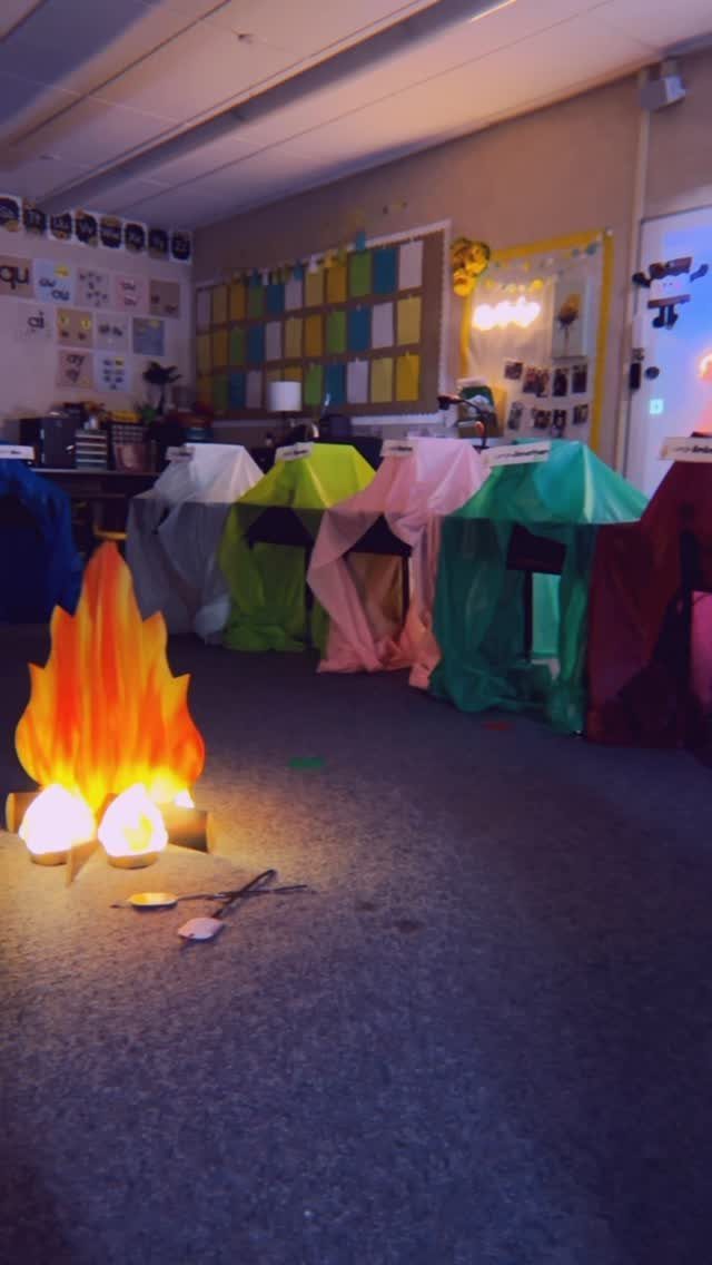 Colorful fabric tents and a glowing artificial campfire in a classroom setting.