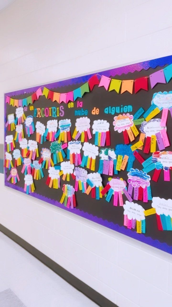 Rainbow-themed bulletin board with colorful paper rainbows and clouds on a black background.