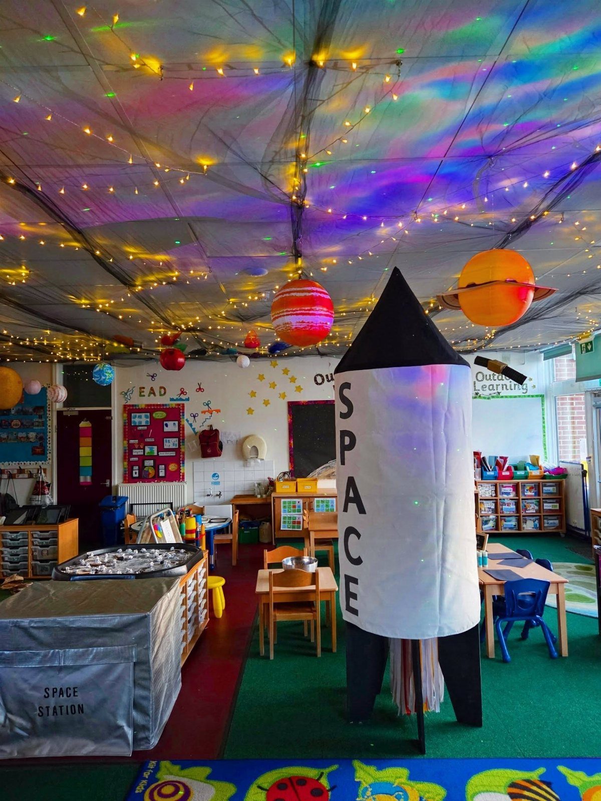 Space themed classroom with a large rocket model, hanging planets, and starry ceiling.