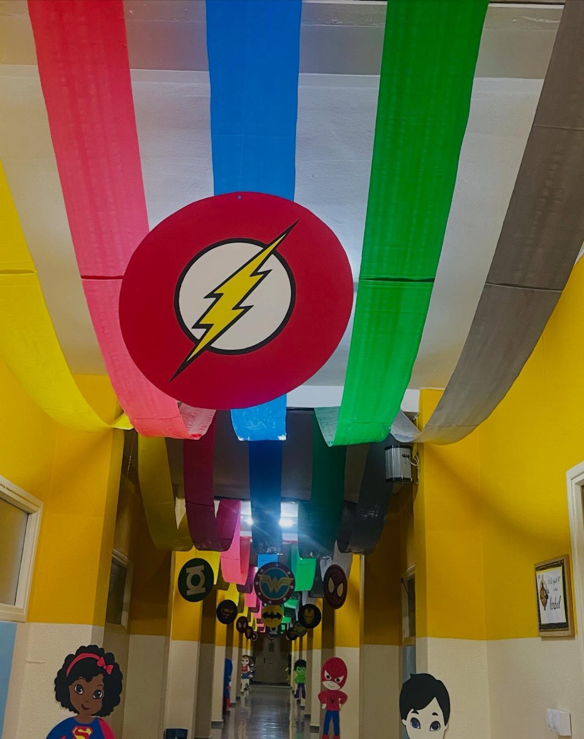 School hallway decorated with colorful ceiling streamers and superhero themed signs and cutouts.