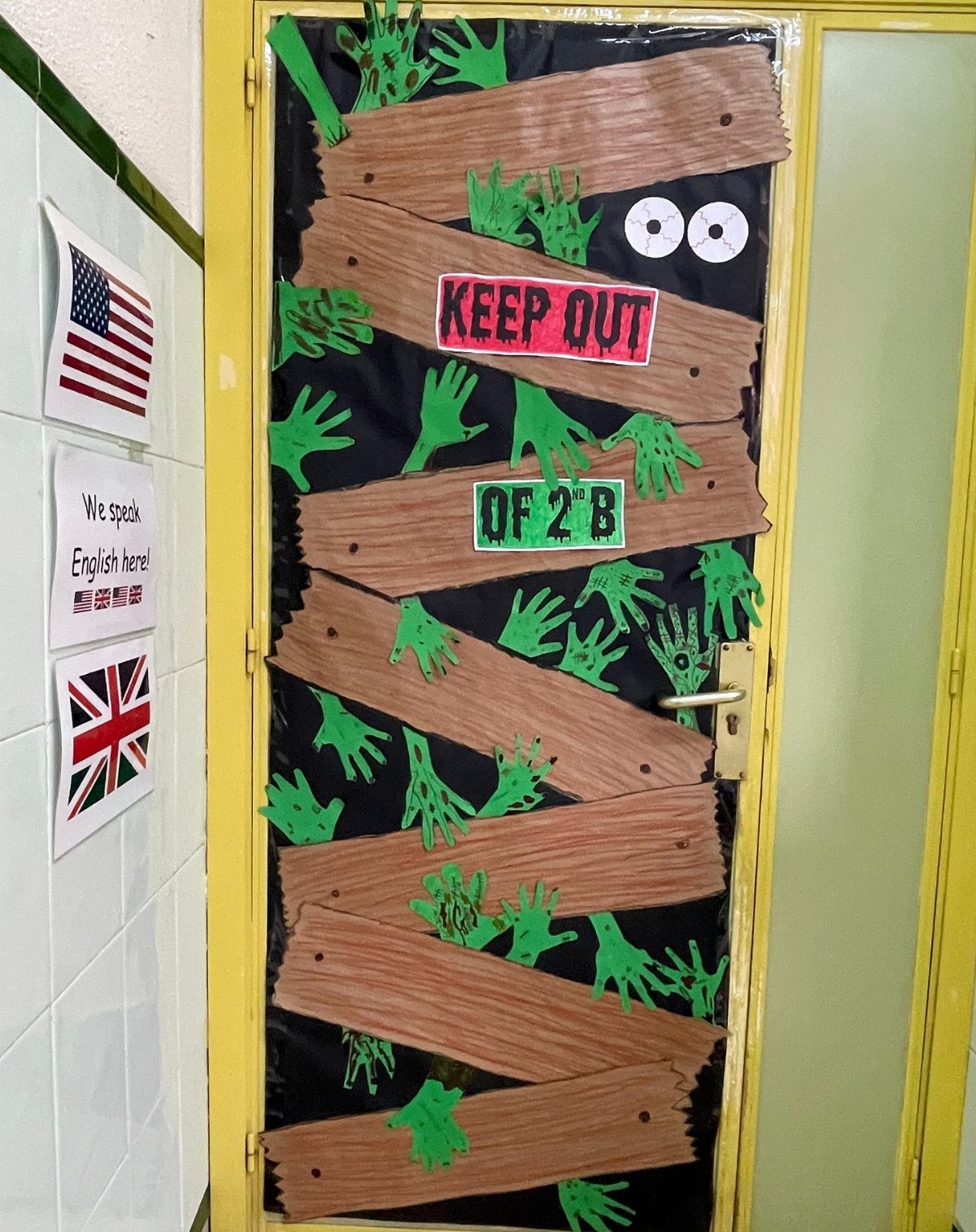Halloween classroom door decorated with zombie hands and brown cardboard wooden planks.