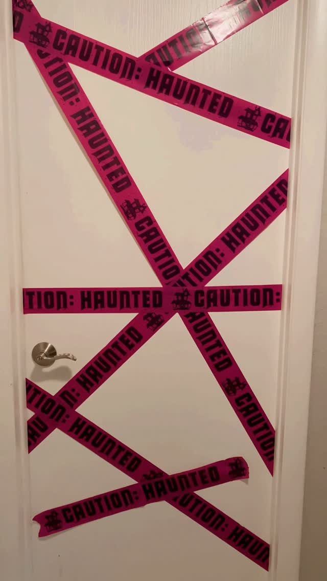 White door decorated with crisscrossing pink haunted caution tape for Halloween.