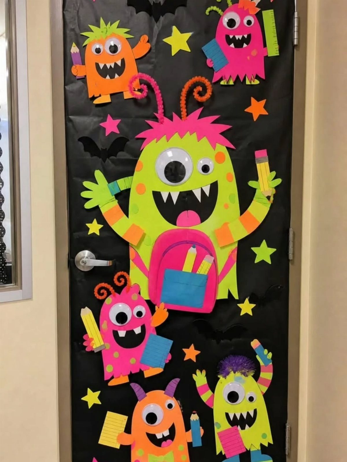 Classroom door decorated with colorful paper monsters, stars, and bats on black background