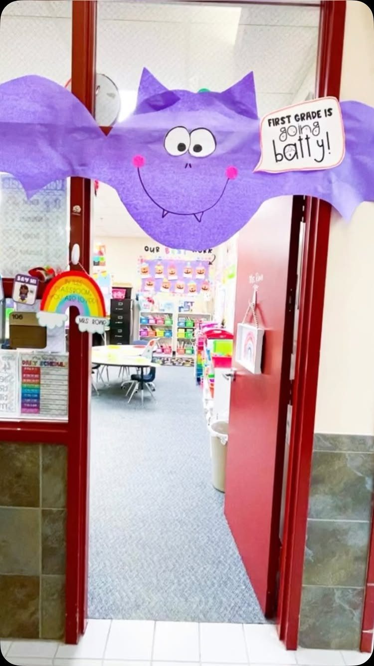 Purple paper bat decoration on a red classroom door frame with a speech bubble.