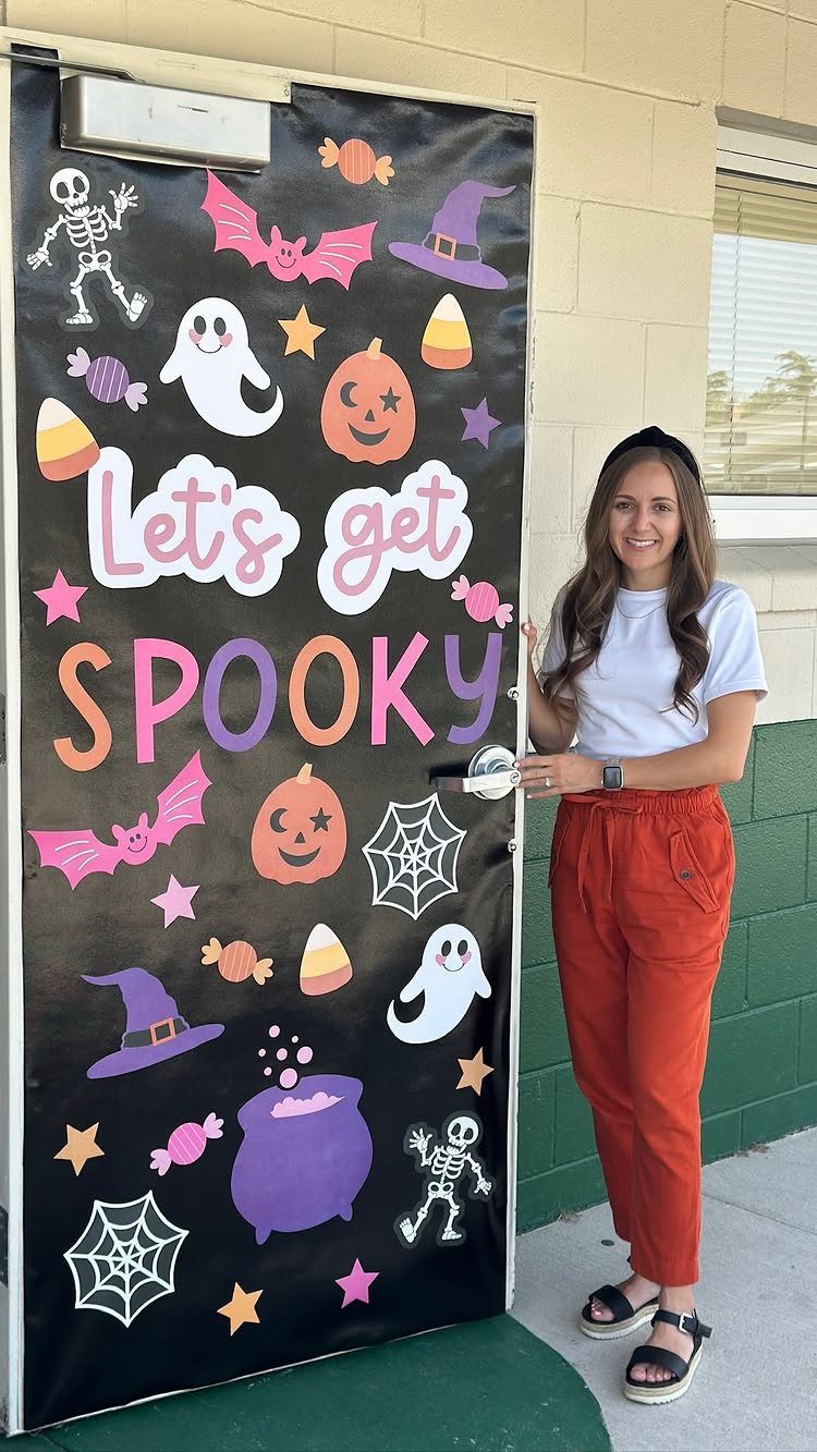 Halloween decorated classroom door with spooky cutouts and a woman standing beside it.