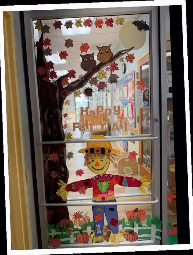 Classroom door decorated with a paper scarecrow, autumn leaves, and a tree.