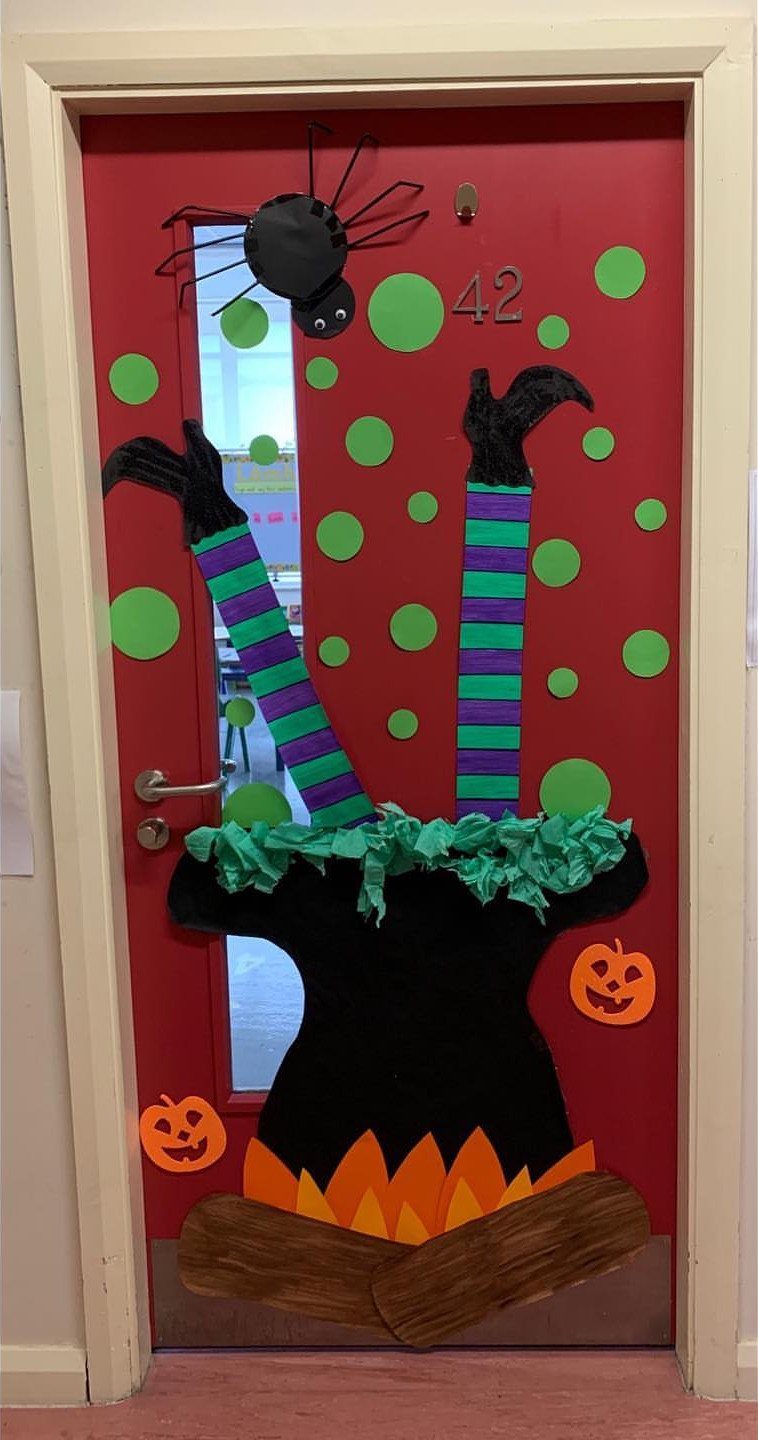 Red classroom door decorated with a black witch's cauldron and striped legs.