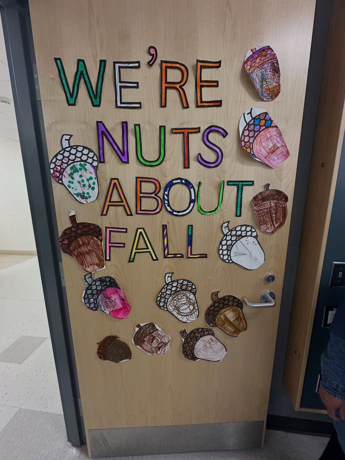 Classroom door decorated with colorful paper acorns and text saying We're Nuts About Fall