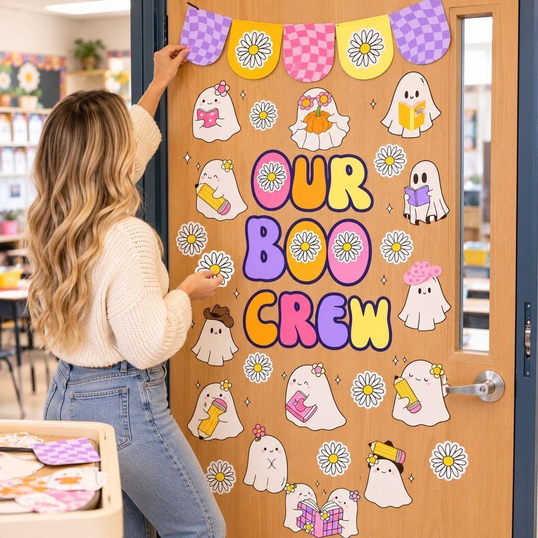 Woman decorating a classroom door with ghosts and 'OUR BOO CREW' text.