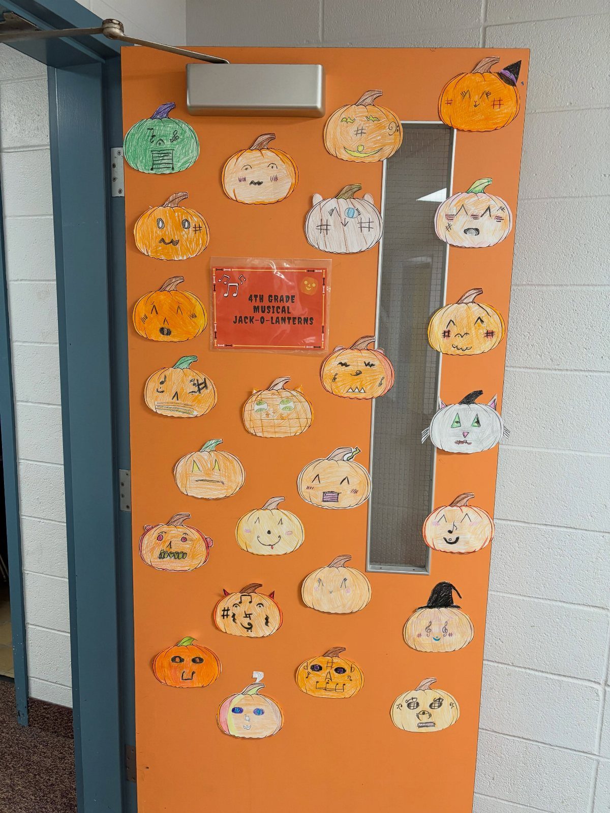 Orange classroom door decorated with many colorful hand-drawn jack-o'-lantern paper cutouts.