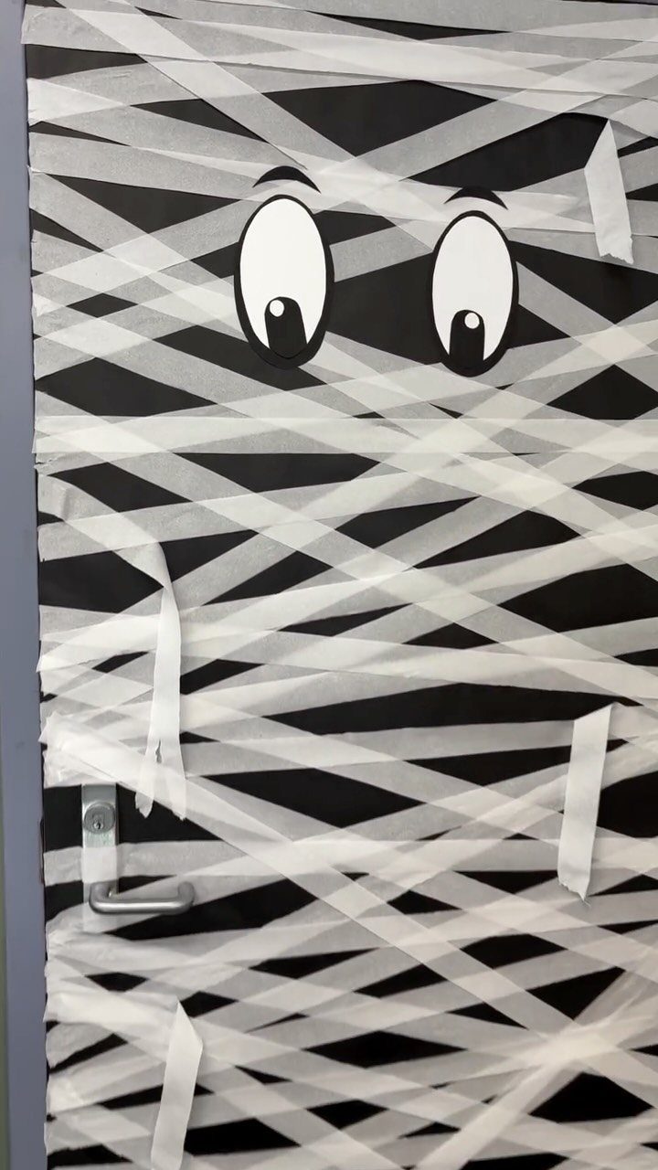Mummy decorated door with white paper strips and large cartoon eyes on black background