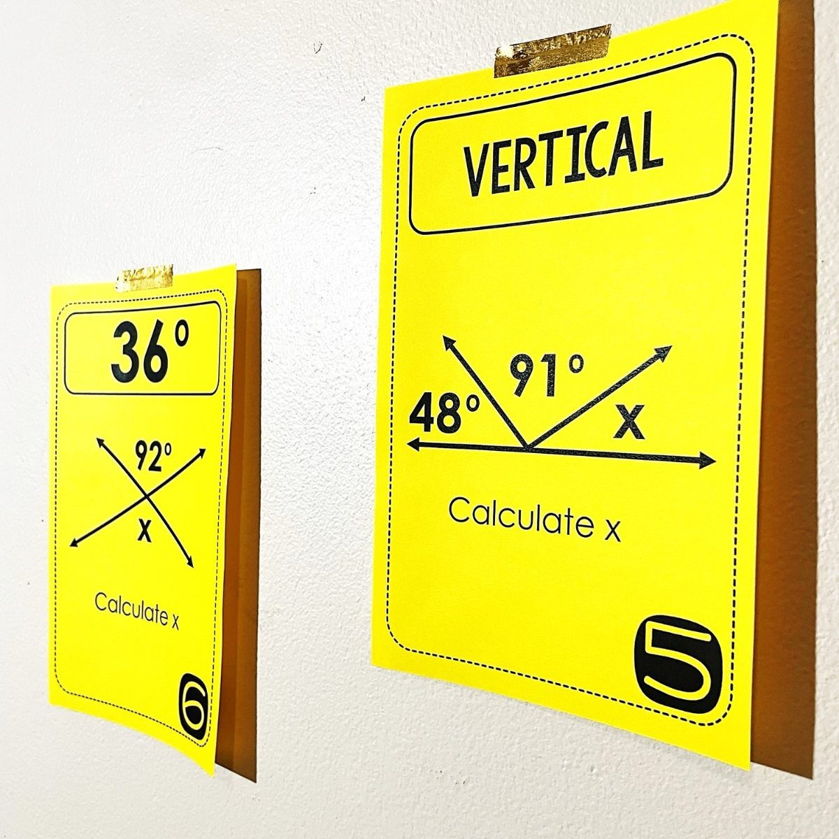 Yellow geometry problem cards taped to a wall for a classroom activity.