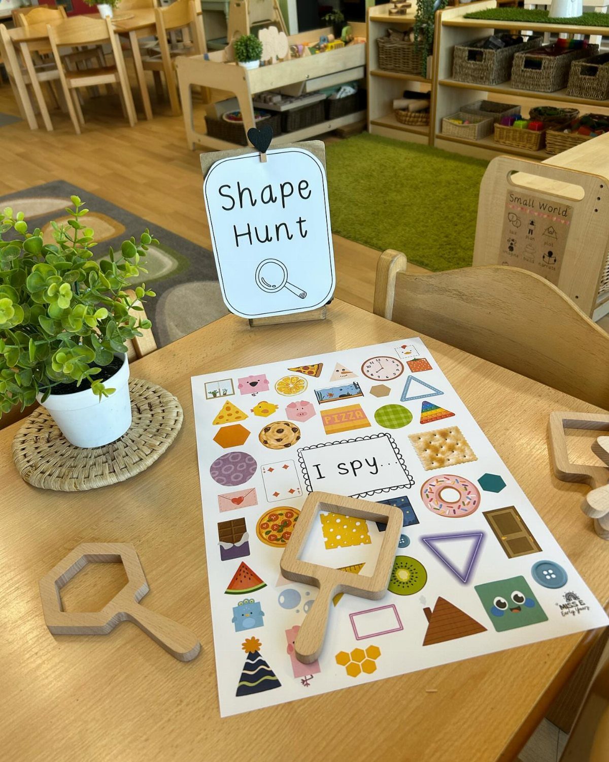 Shape hunt activity sheet and wooden magnifying glasses on a classroom table.