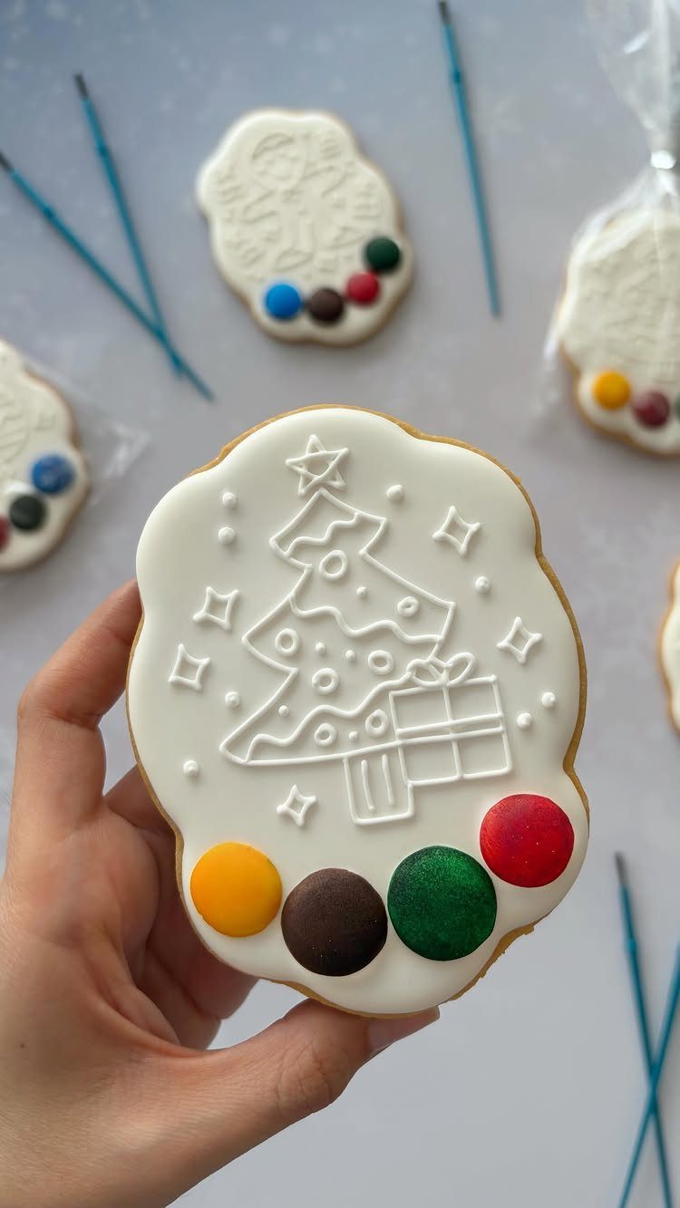 Hand holding a white Christmas tree cookie with colorful icing paint dots