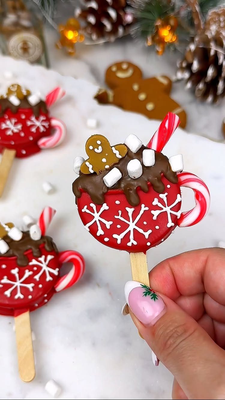 Red mug shaped cookies decorated with chocolate, marshmallows, and candy canes on marble.