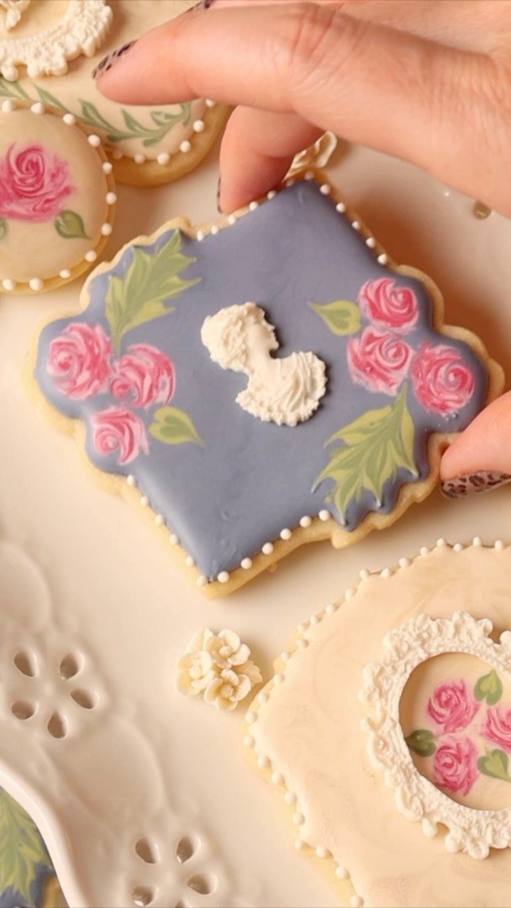 Hand holding a blue sugar cookie decorated with pink roses and green leaves