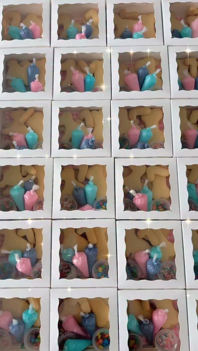 White treat boxes with windows containing cookies and colorful icing piping bags.