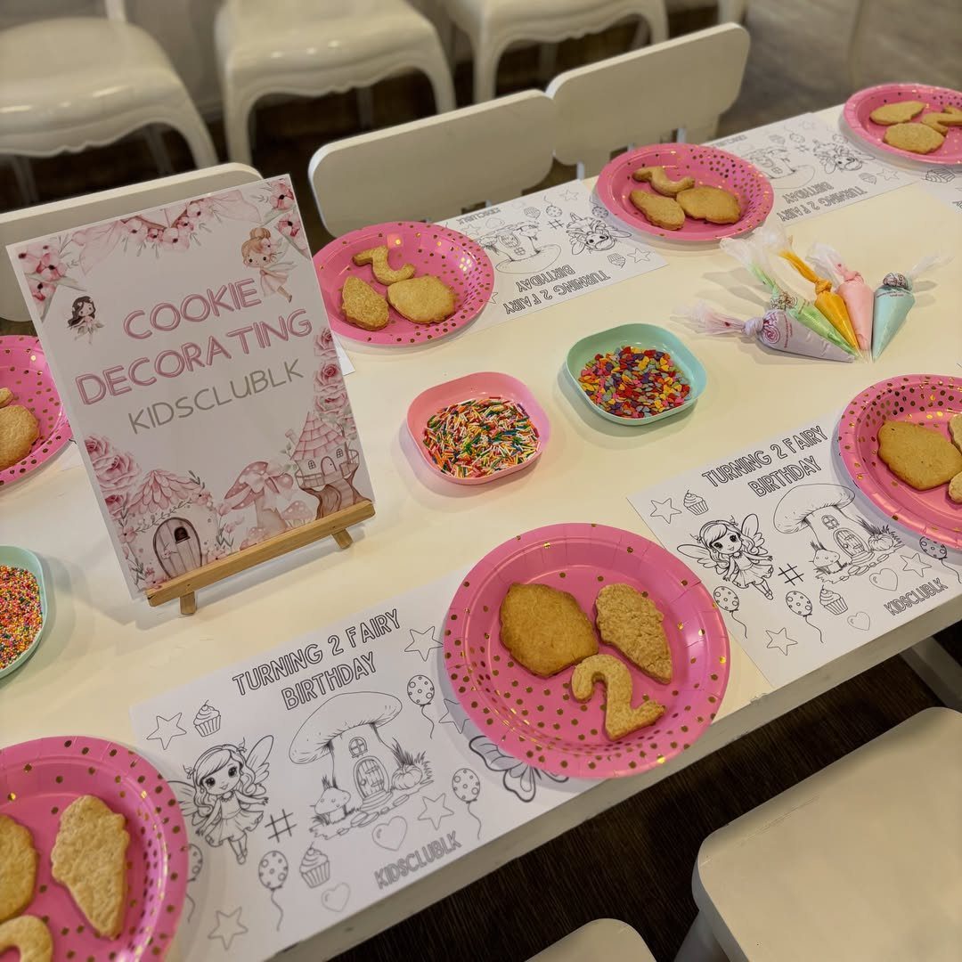 Cookie decorating table with pink plates, sprinkles, and fairy themed party decorations.