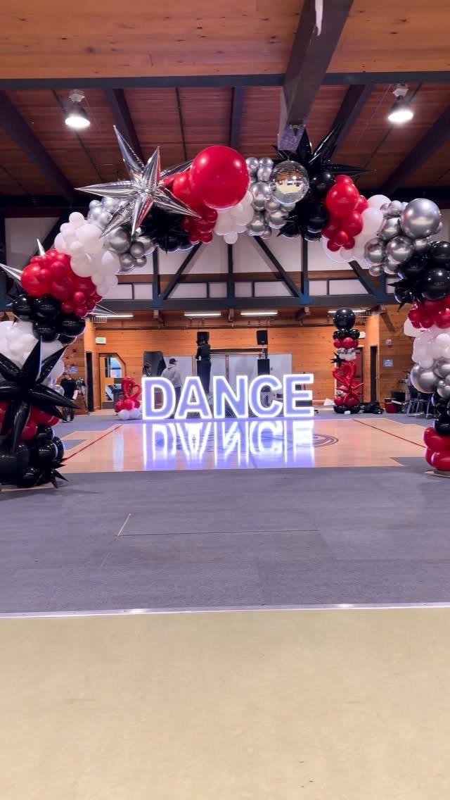 Balloon arch in red, black, and silver framing illuminated DANCE letters on a floor.