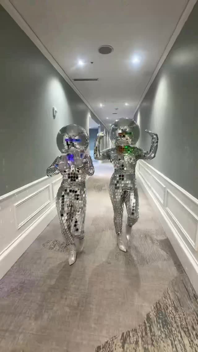 Two people in mirrored disco ball suits posing in a hotel hallway
