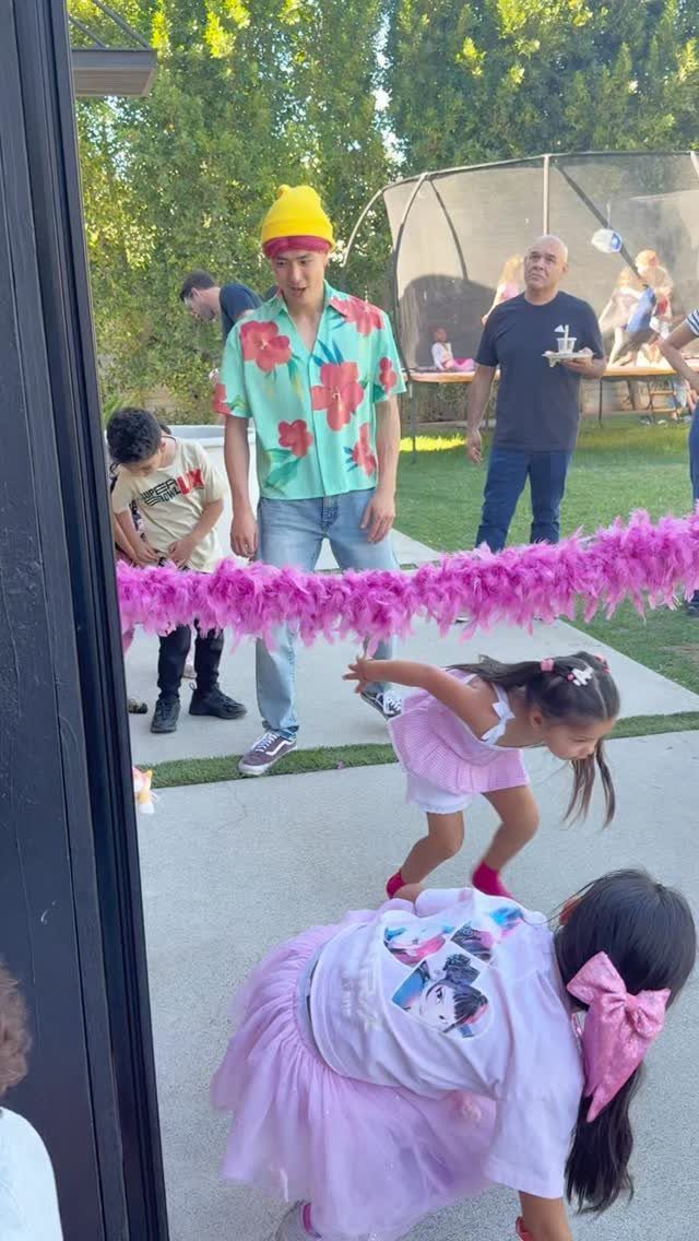 Children leaning back to go under a pink feather boa during a limbo contest.