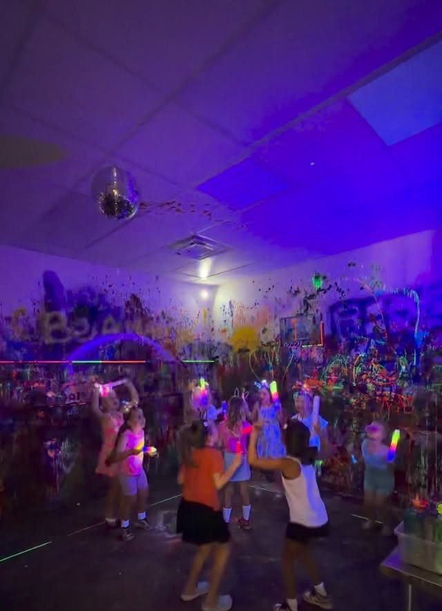 Children dancing with neon glow sticks under a disco ball in a purple room