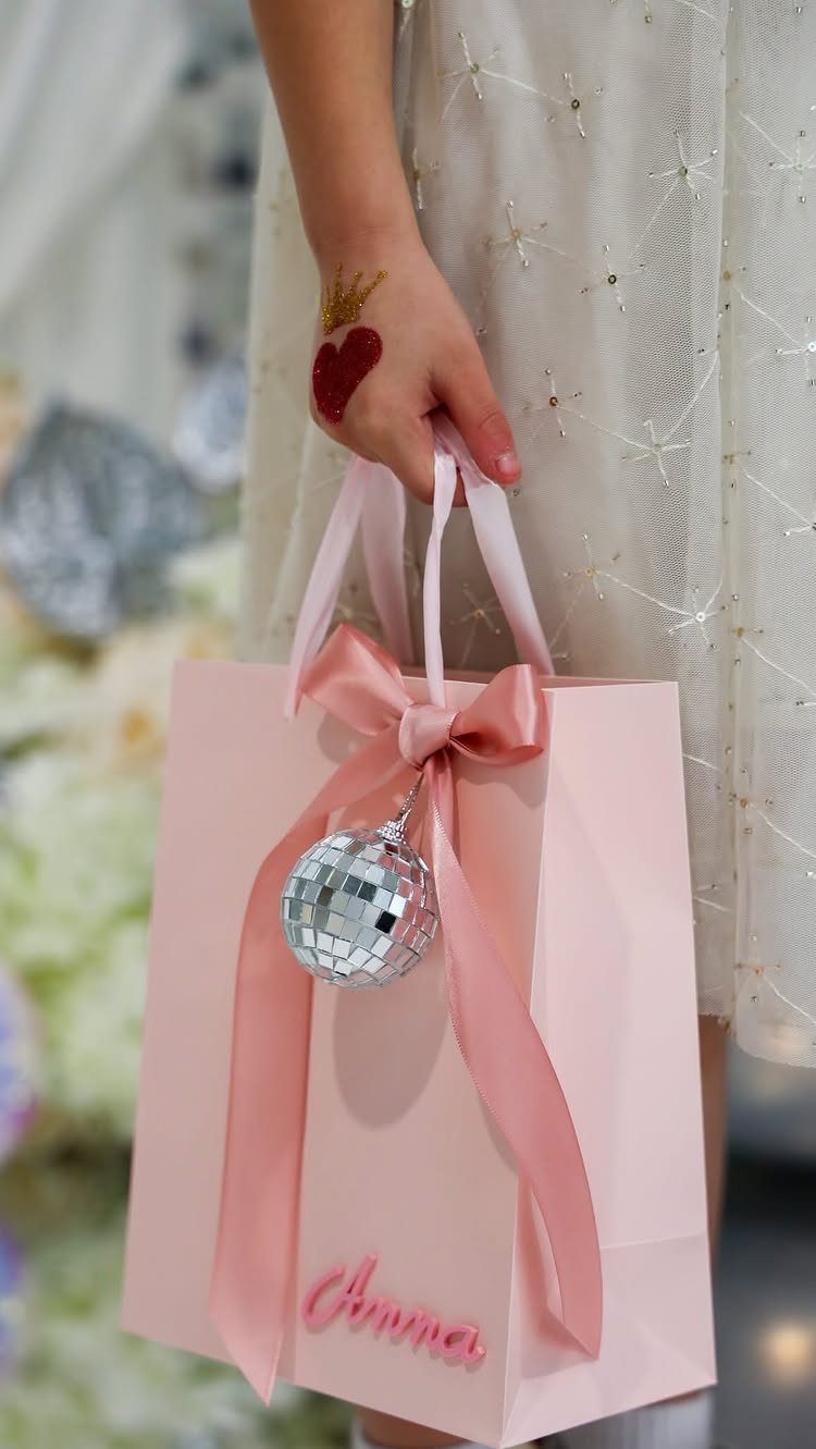 Pink gift bag with a disco ball ornament held by a person.