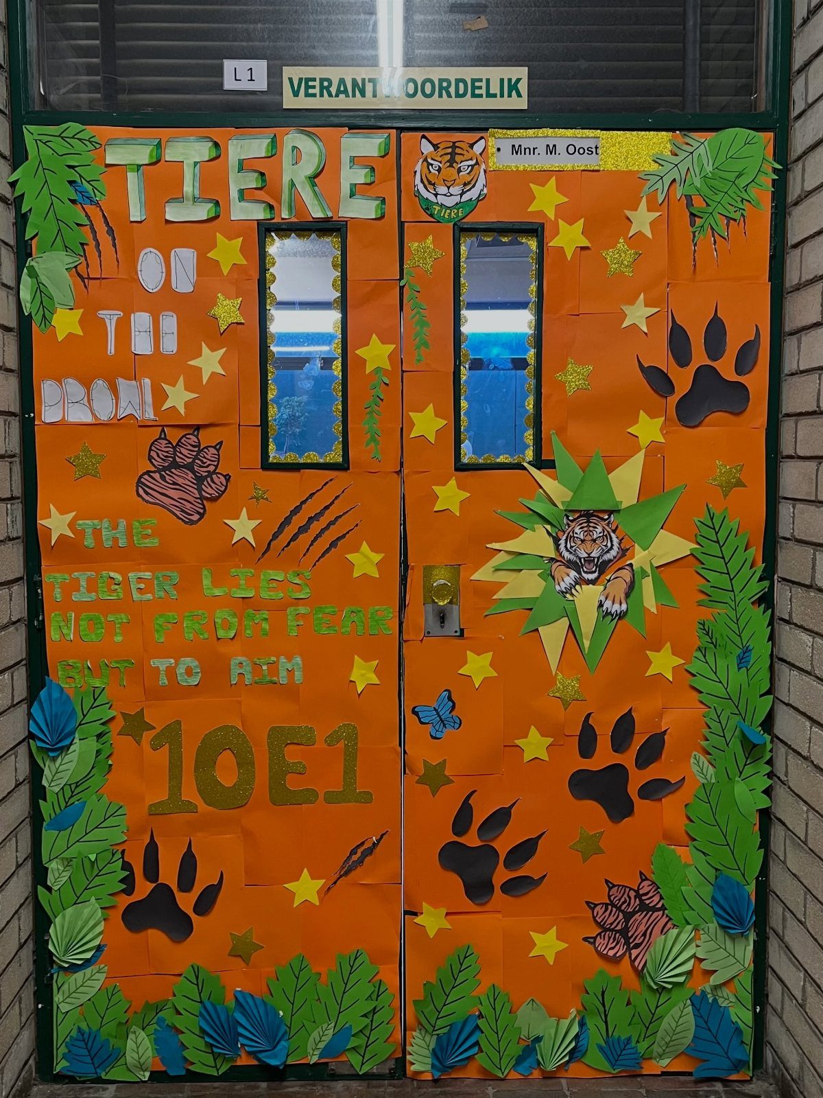 Orange classroom door decorated with tiger faces, paw prints, and green jungle leaves.