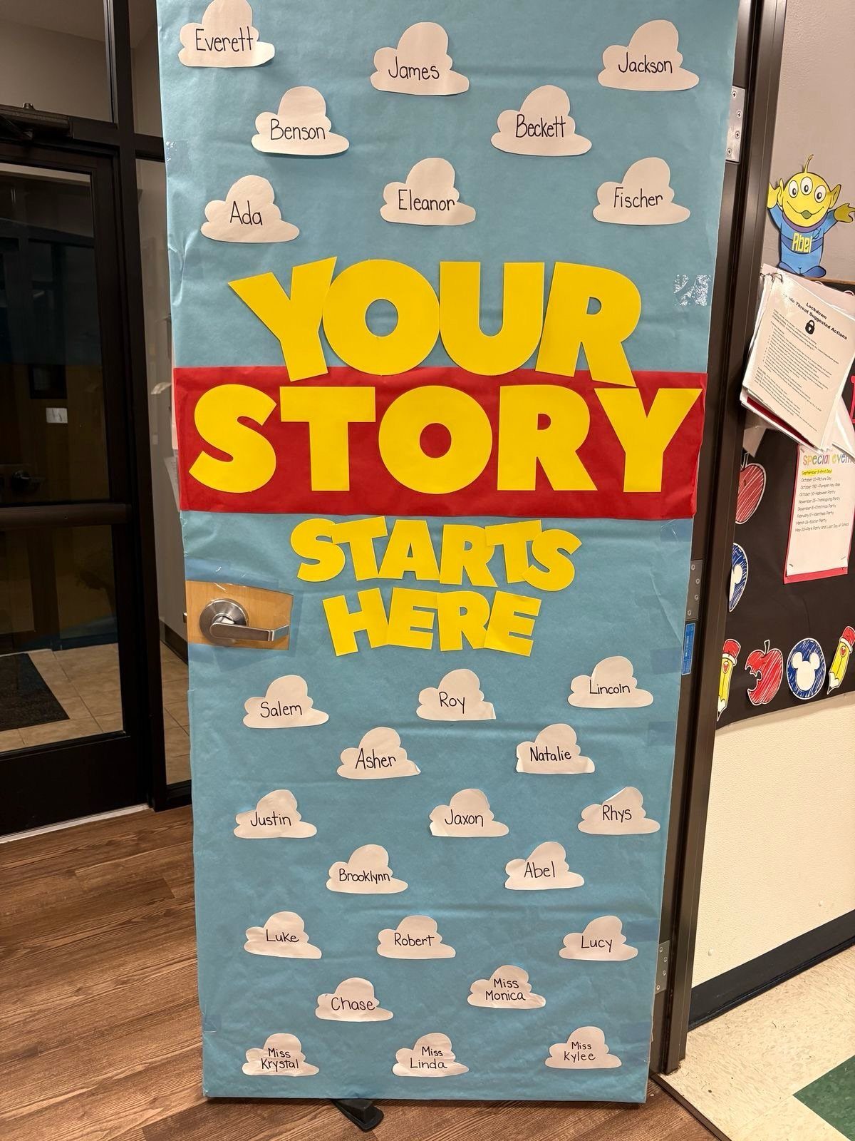 Classroom door decorated with blue paper, yellow text, and name clouds for students.