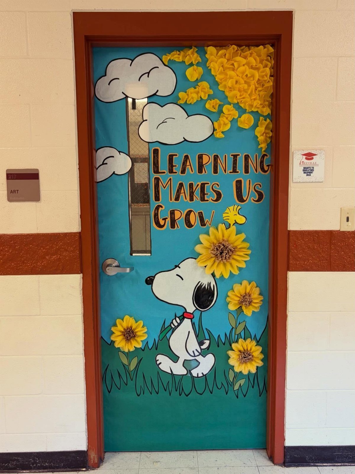 Classroom door decorated with Snoopy, yellow sunflowers, and learning growth motivational text.