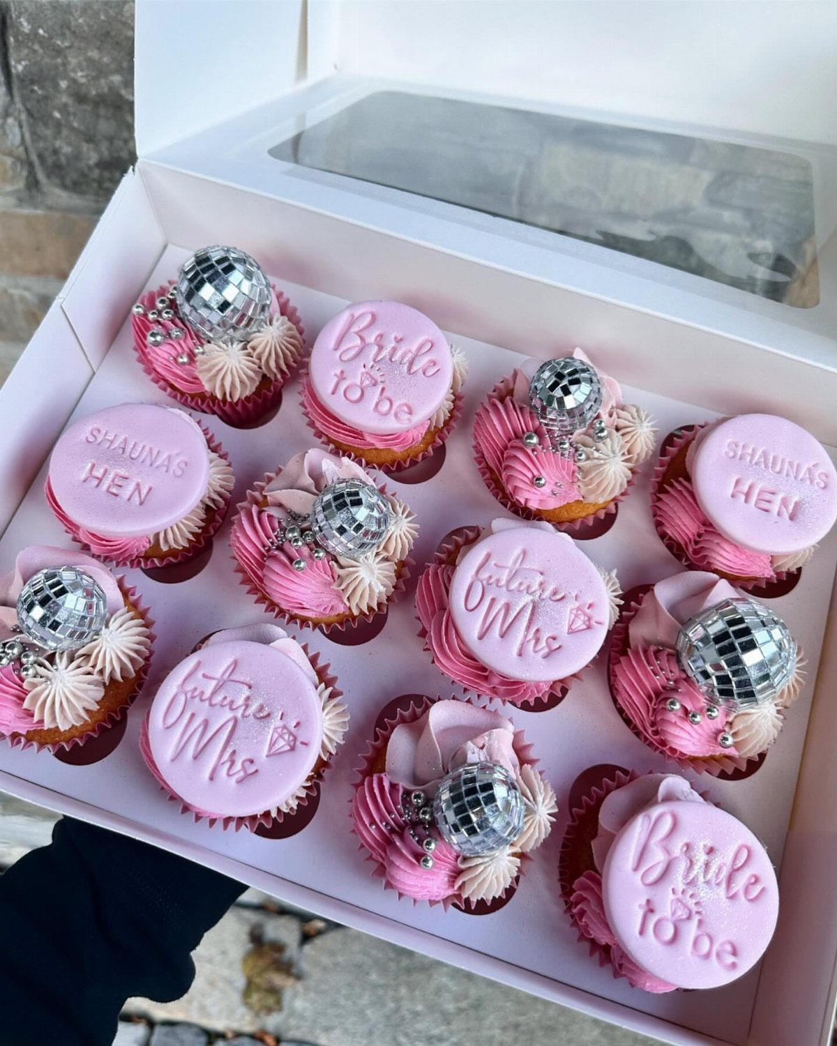 Cupcakes with pink frosting topped with miniature disco balls and bridal text discs.