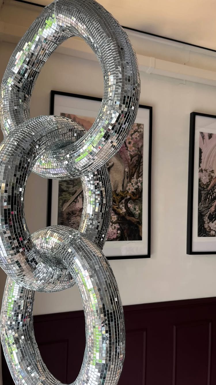 Interlocking mirrored disco ball rings hanging against a white wall with framed art.