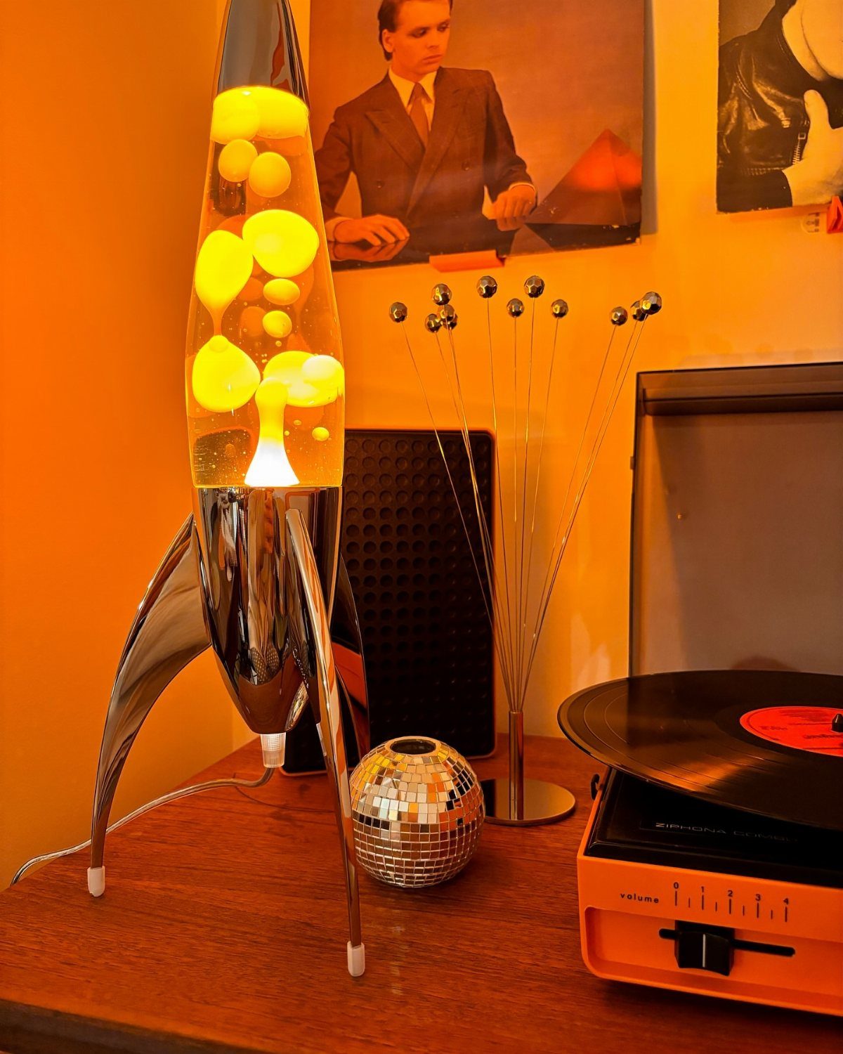 Rocket-shaped lava lamp with yellow wax next to a small disco ball and record player