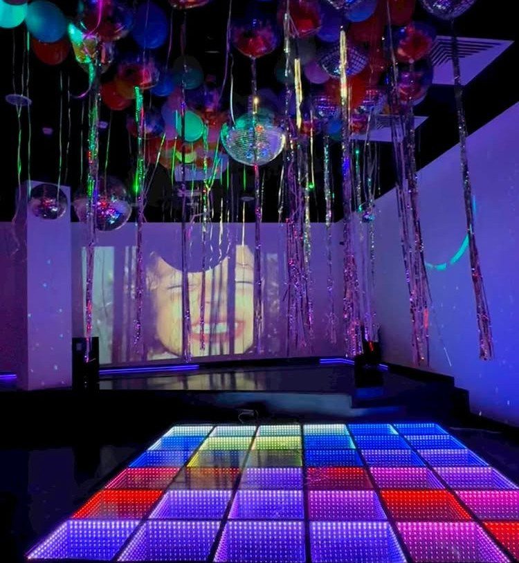 Colorful illuminated dance floor with disco balls and balloons in a party room