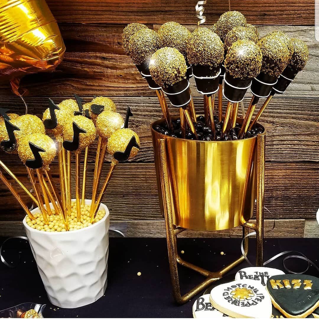 Microphone shaped cake pops with gold glitter in a gold bucket and white cup.